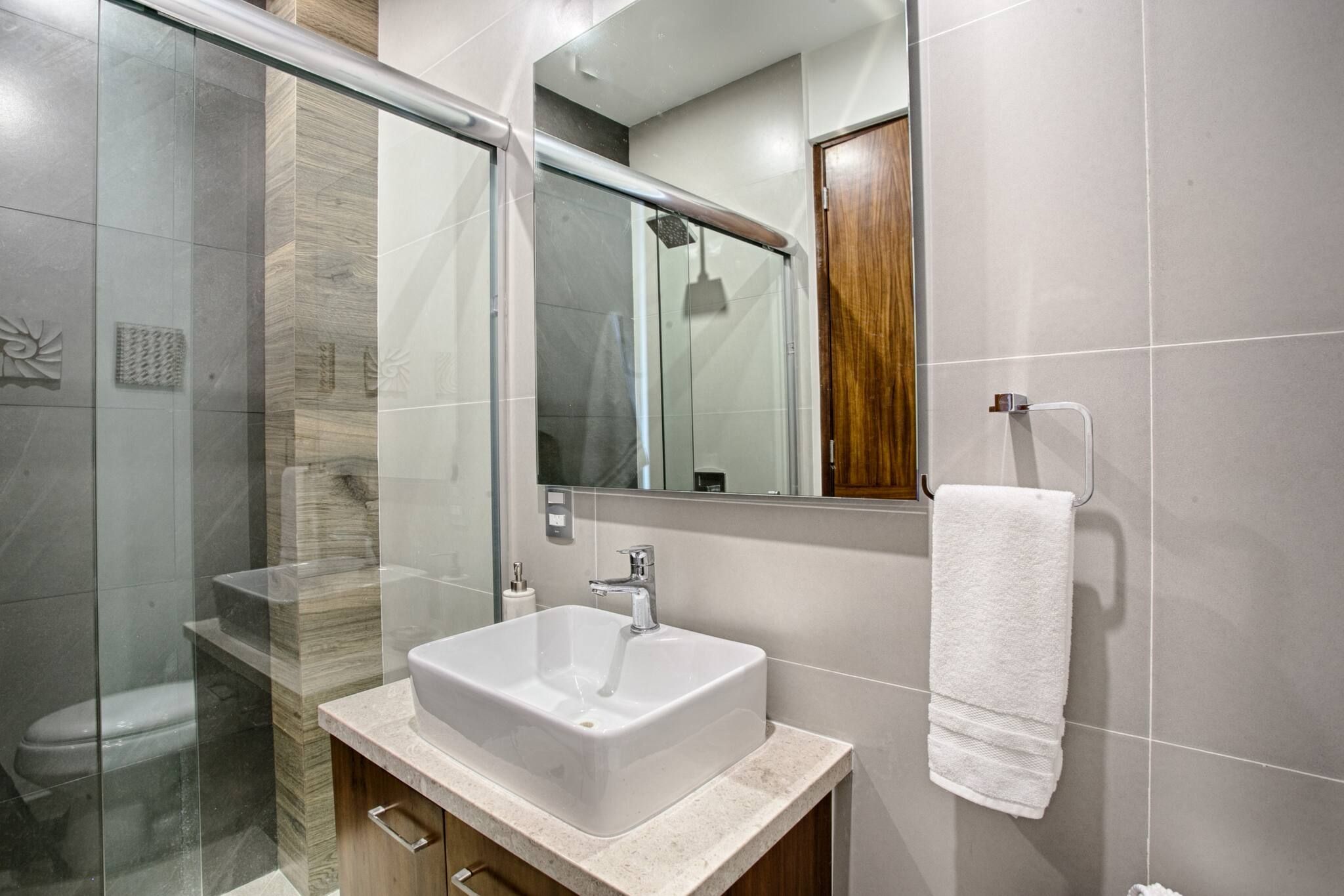 A modern bathroom with a glass shower enclosure, a white sink, and a wooden cabinet.