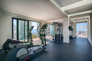 A gym with exercise equipment, large windows, and a view of the sea.