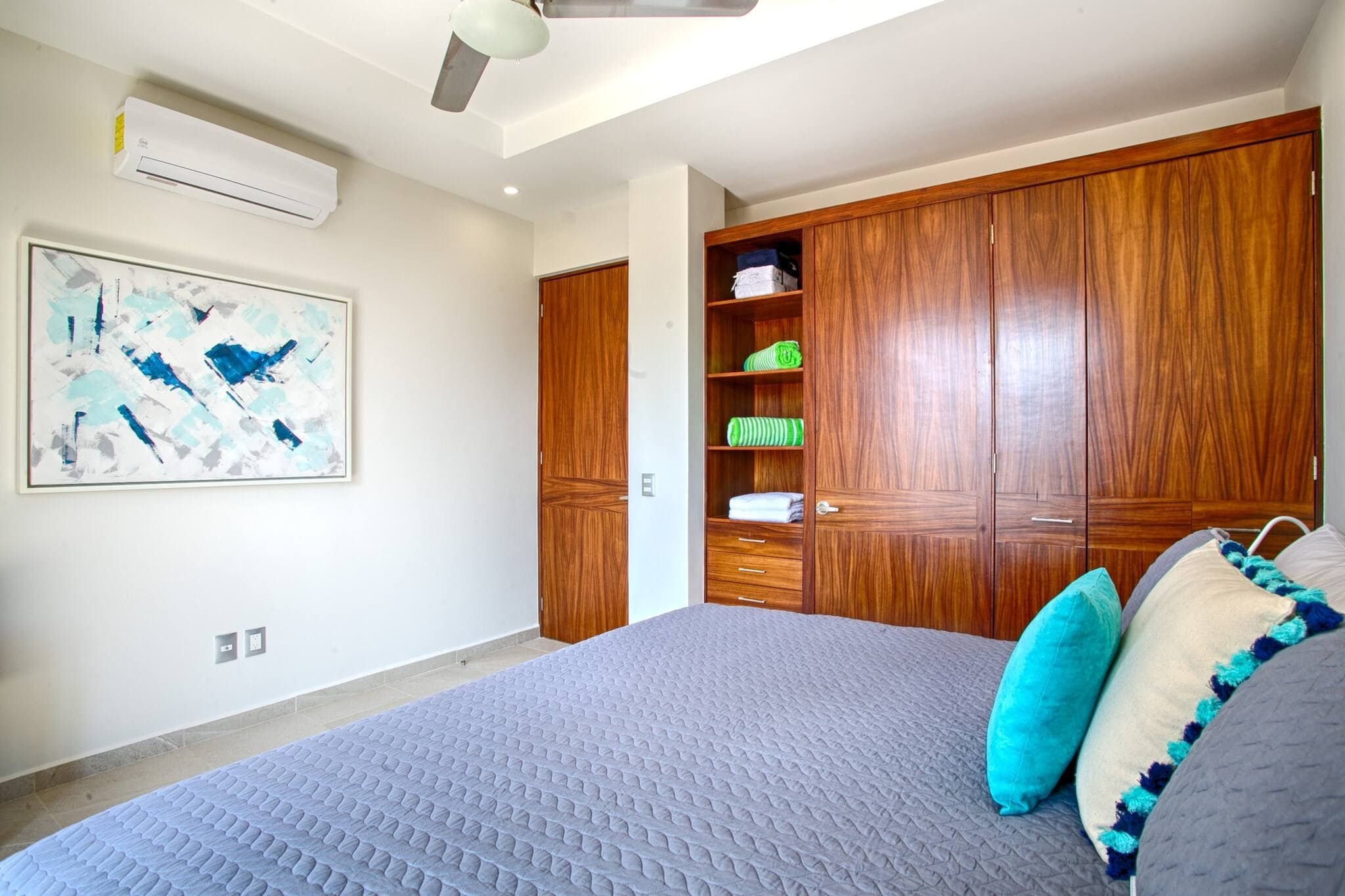 A bedroom with a large bed, a wardrobe, a shelf with towels, and an air conditioning unit.