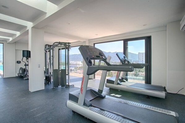 A gym with treadmills, weight machines, and a view of mountains through large windows. - Steps from Beach | Pool + Hot tub + Gym + Balcony (Puerto Vallarta)