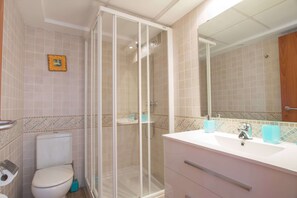 Un baño con inodoro, cabina de ducha y lavamanos con espejo.