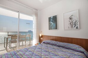Habitación de hotel con una cama, un balcón con mesa y sillas, y dos obras de arte colgadas en la pared.
