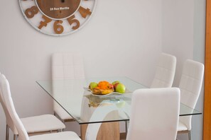 A dining area with a glass table, white chairs, and a fruit bowl. - Apartment Barlovento - PlusHolidays (Calpe)