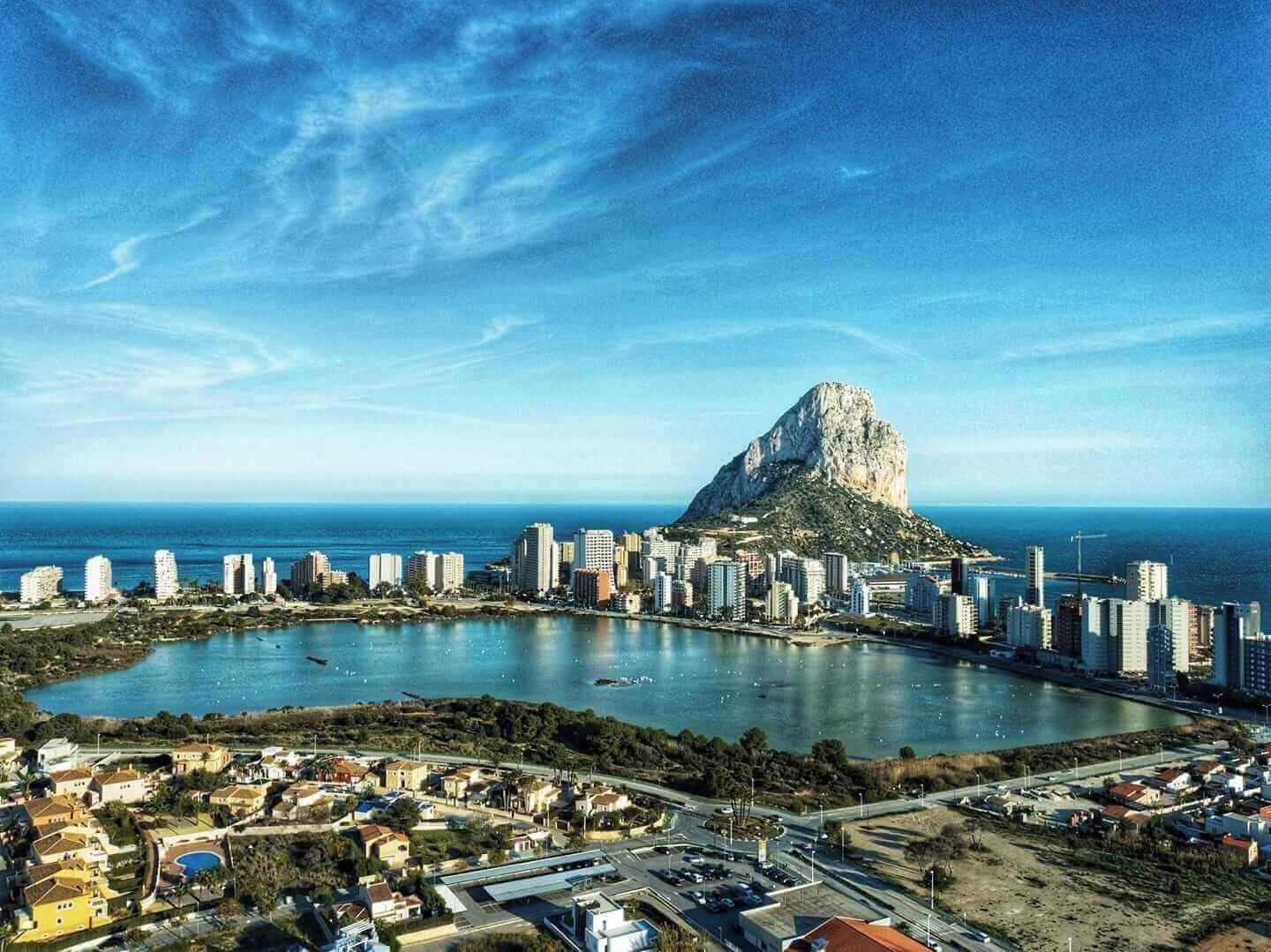 A coastal cityscape with a prominent mountain-like structure, a marina with boats, and a mix of residential and commercial buildings.