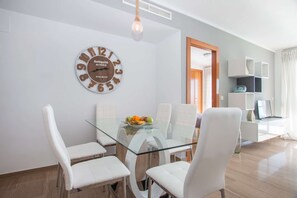 Un espace repas moderne avec une table en verre et des chaises blanches, une horloge décorative et une vue sur le salon.