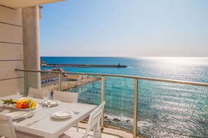 Un balcón con mesa lista para comer, con vista al mar azul y un muelle.