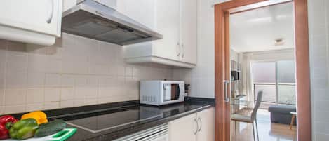 Una cocina moderna con armarios blancos, encimera negra y microondas.