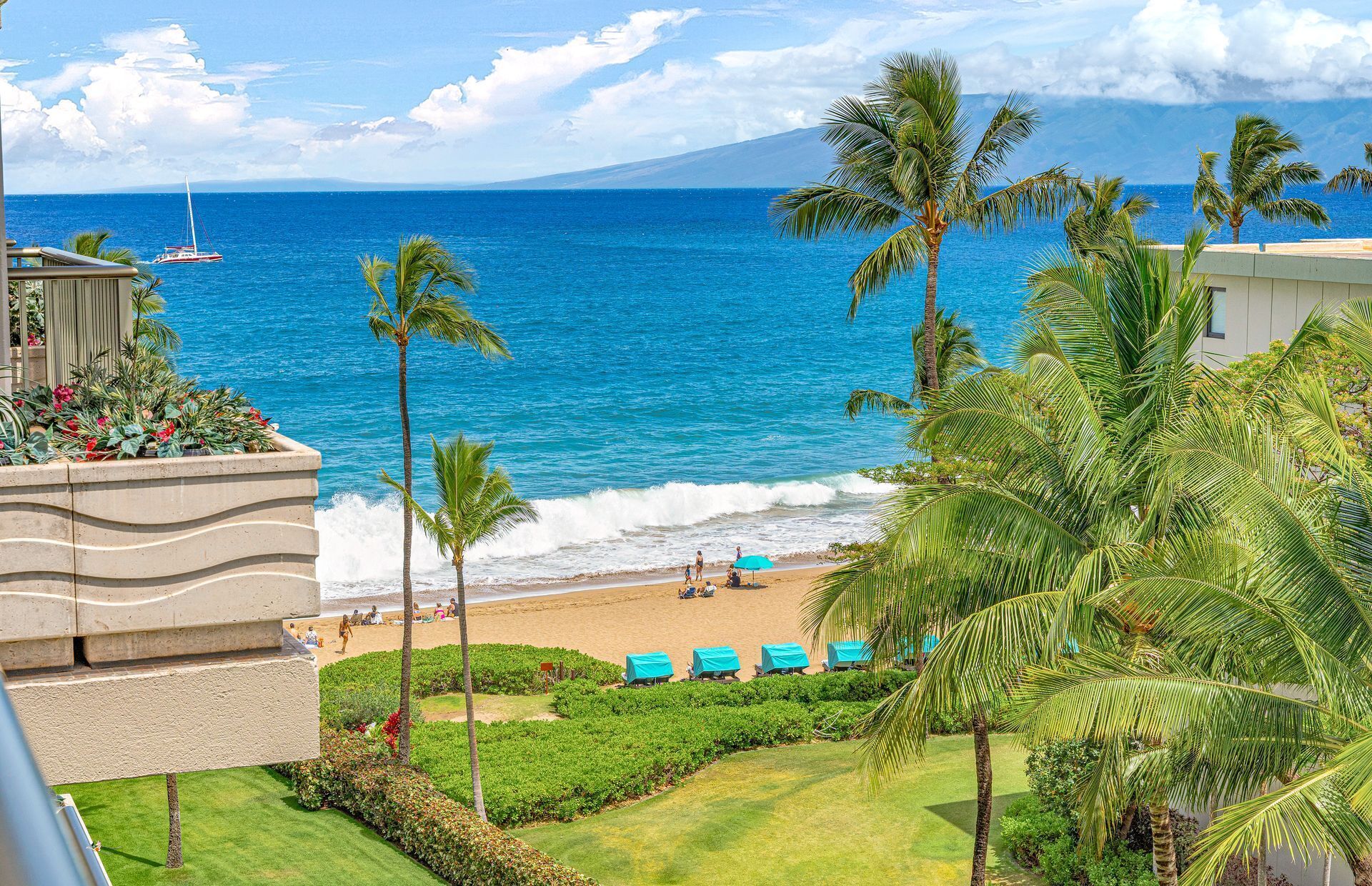 A beachfront hotel with a view of the ocean, palm trees, and a beach with lounge chairs.
