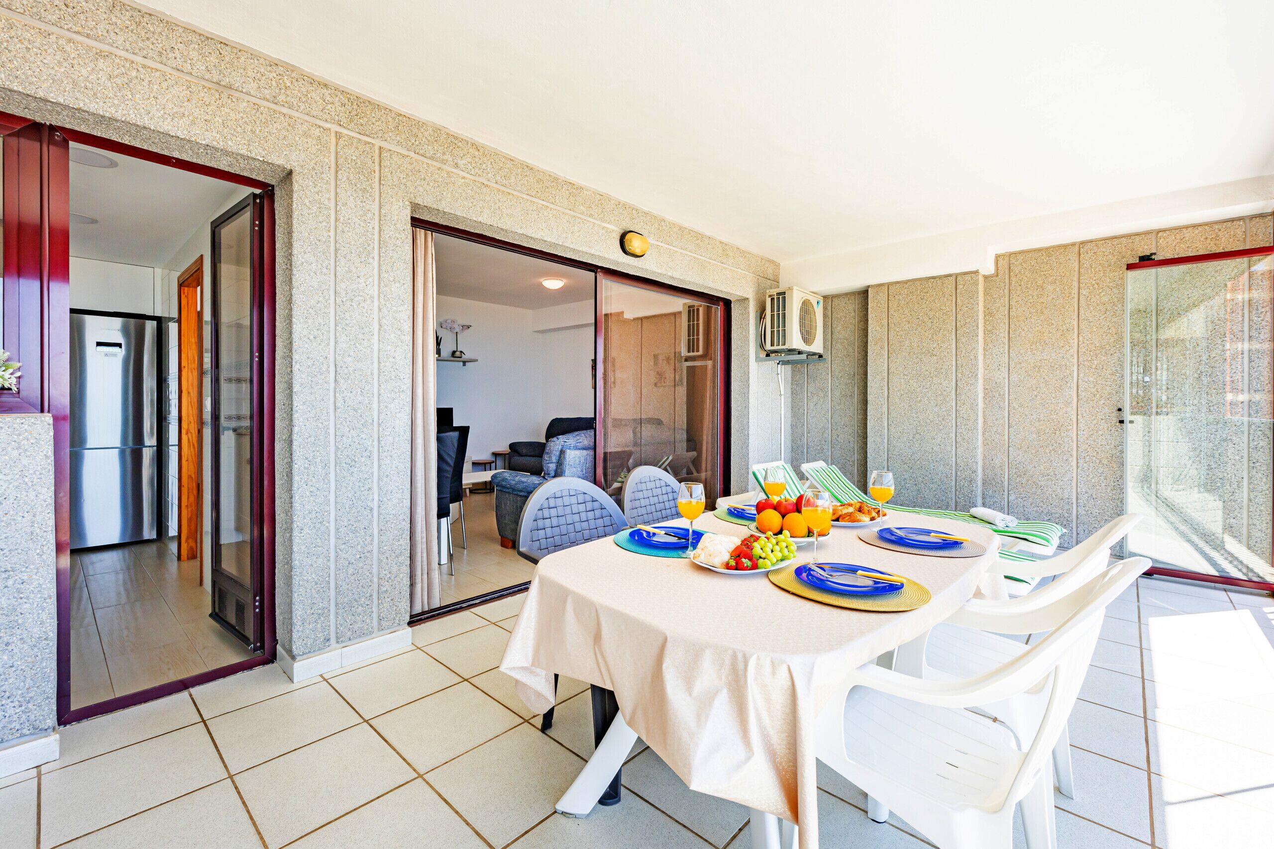 Un comedor con una mesa preparada para dos, una cocina al fondo y un ventanal corredero que da a otra habitación.