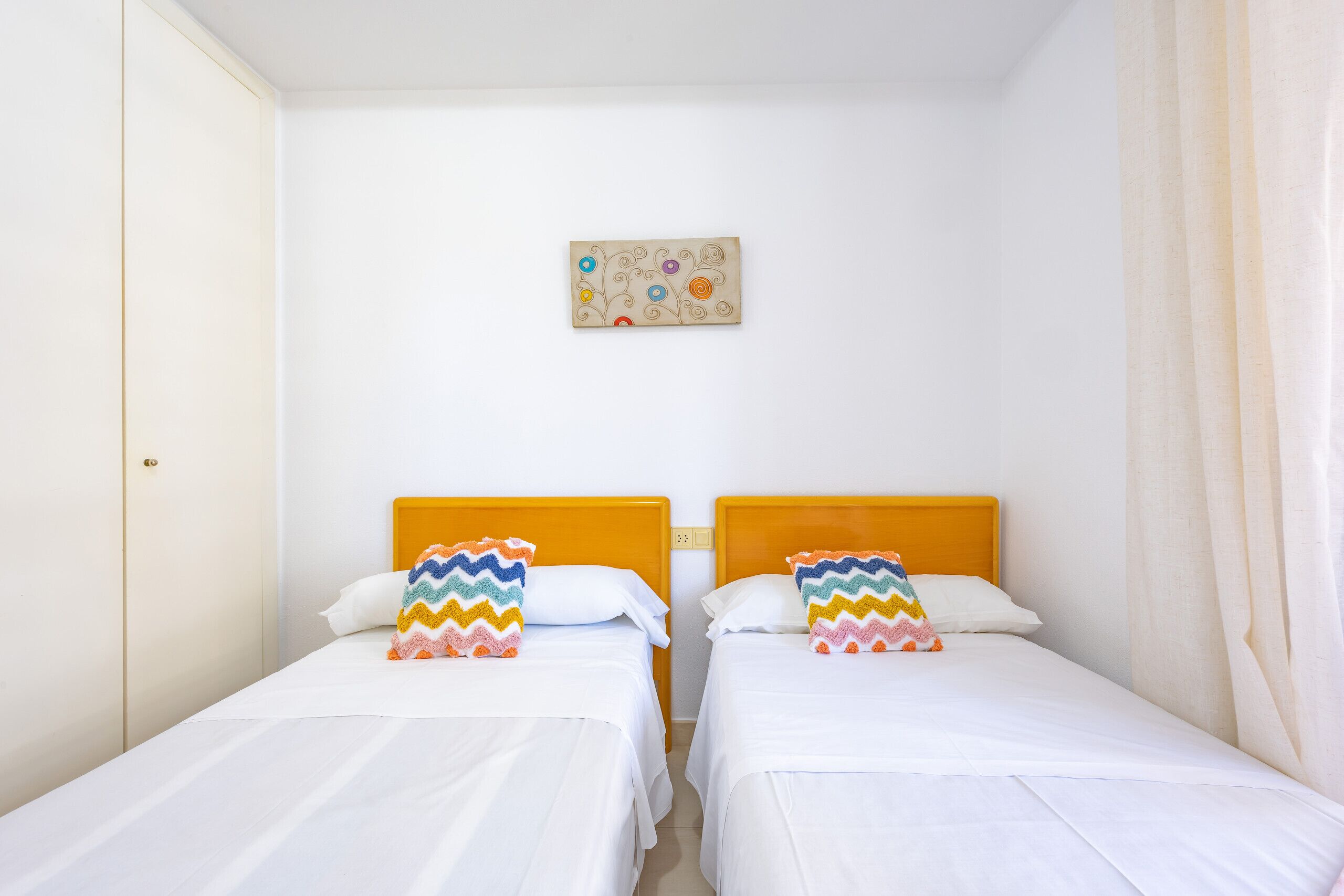 A room with two single beds, each with a wooden headboard and white bedding. There is a small artwork on the wall above the beds.