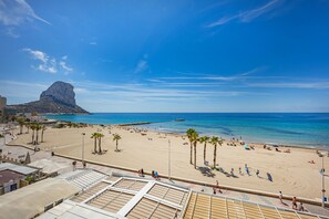 A beach with palm trees, a rocky outcrop, and a clear blue sky. - Apartment Calpeplaya - PlusHolidays (Calpe)