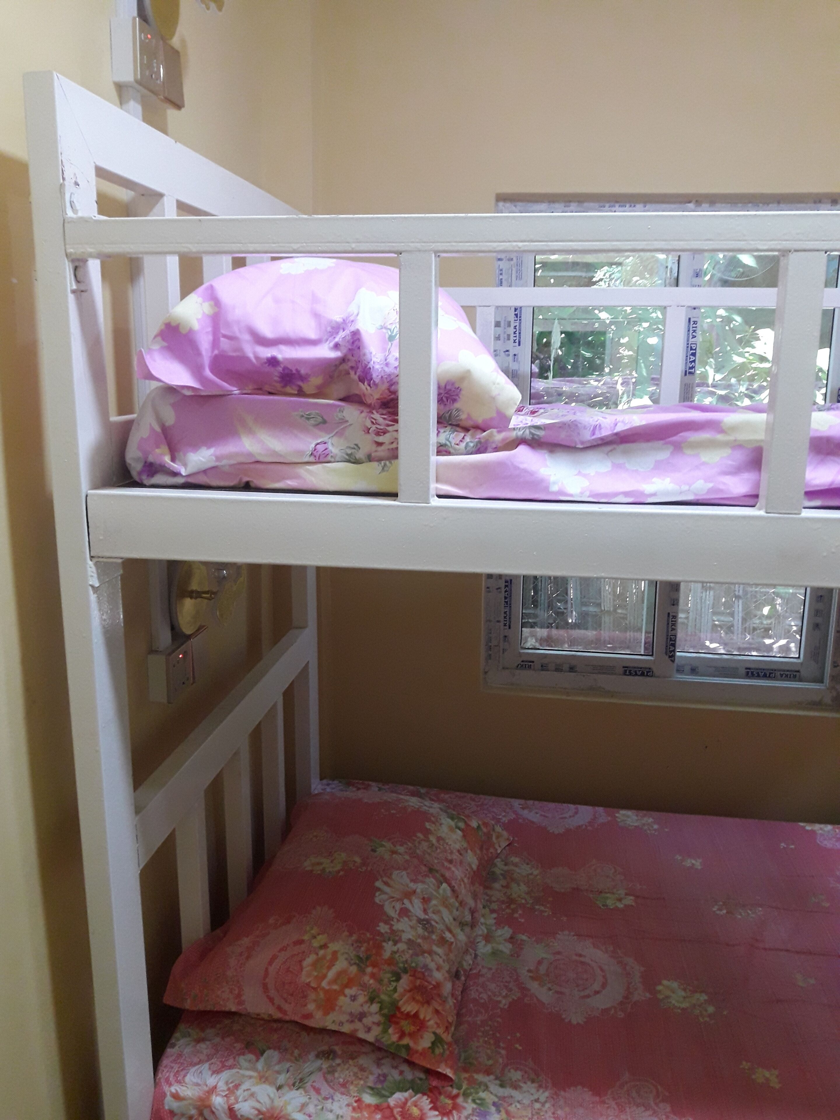 A bunk bed with floral bedding, a window with a view, and a wall-mounted light switch.