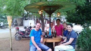 A group of people seated around a round table under a canopy with hanging lights. - My Family - Hostel (Nyaung-U)
