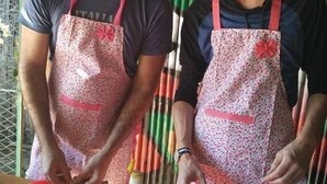 Two individuals standing in front of a bamboo backdrop, wearing aprons, with a table in front of them containing various food items and cooking utensils. - My Family - Hostel (Nyaung-U)
