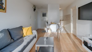 A modern living room with a grey sofa, a small white table, and a dining area with white chairs and a table.