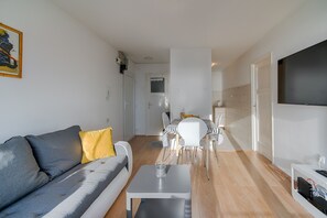 Una sala de estar moderna con un sofá gris, una mesita blanca y un comedor con sillas y una mesa blancos.