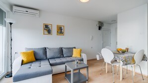 A modern living room with a grey sectional sofa, a small side table, and a dining area with a zebra-striped tablecloth.