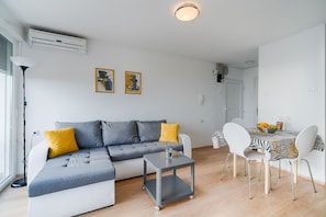 Una sala de estar moderna con un sofá seccional gris, una mesita auxiliar y un comedor con mantel a rayas de cebra.