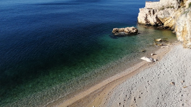 A coastal beach with clear water and rocky cliffs.