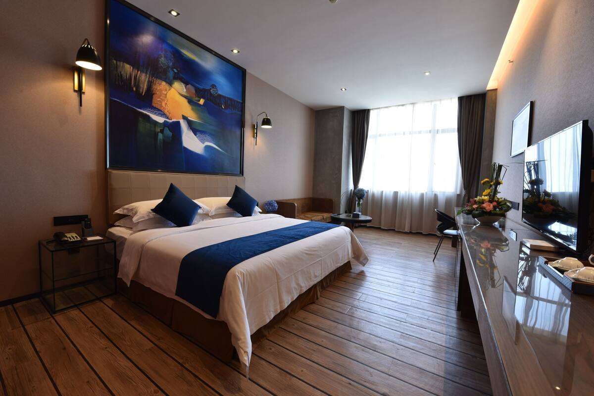 Habitación de hotel con una cama grande, un televisor de pantalla plana, piso de madera y un cuadro en la pared.