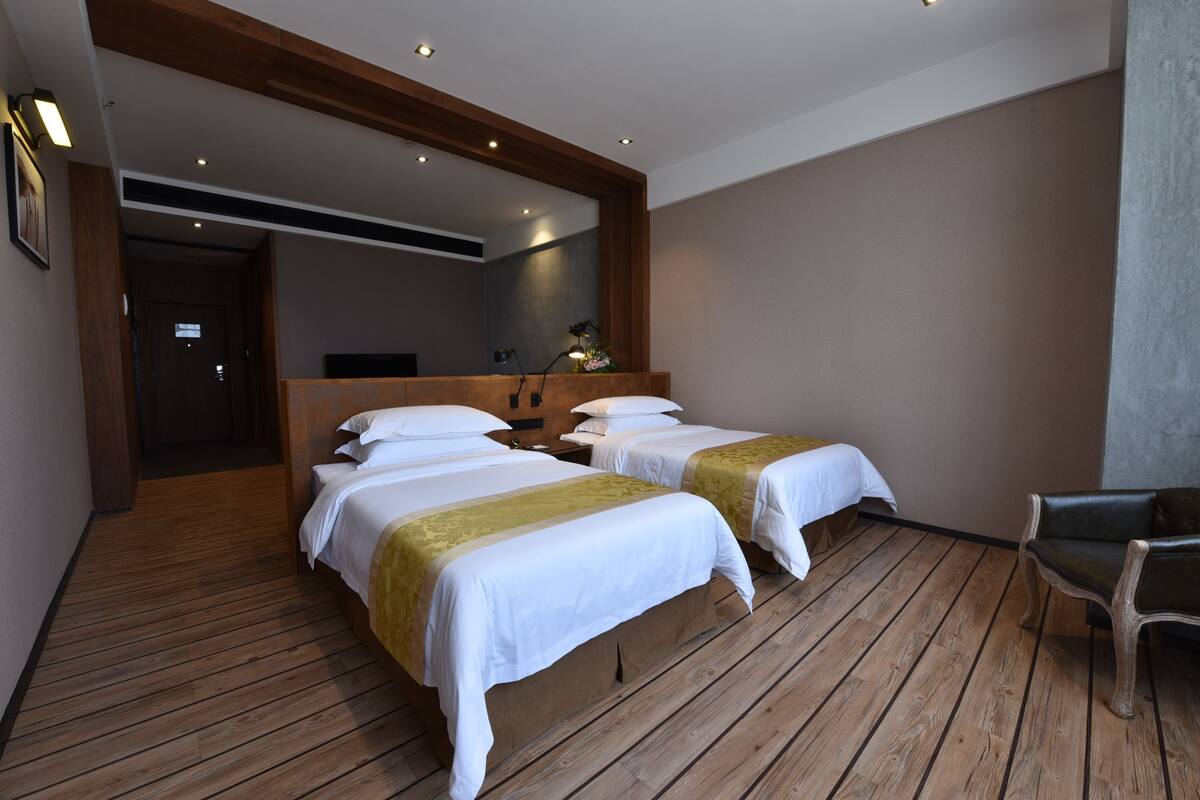 Habitación de hotel con dos camas, piso de madera, un espejo y una silla.