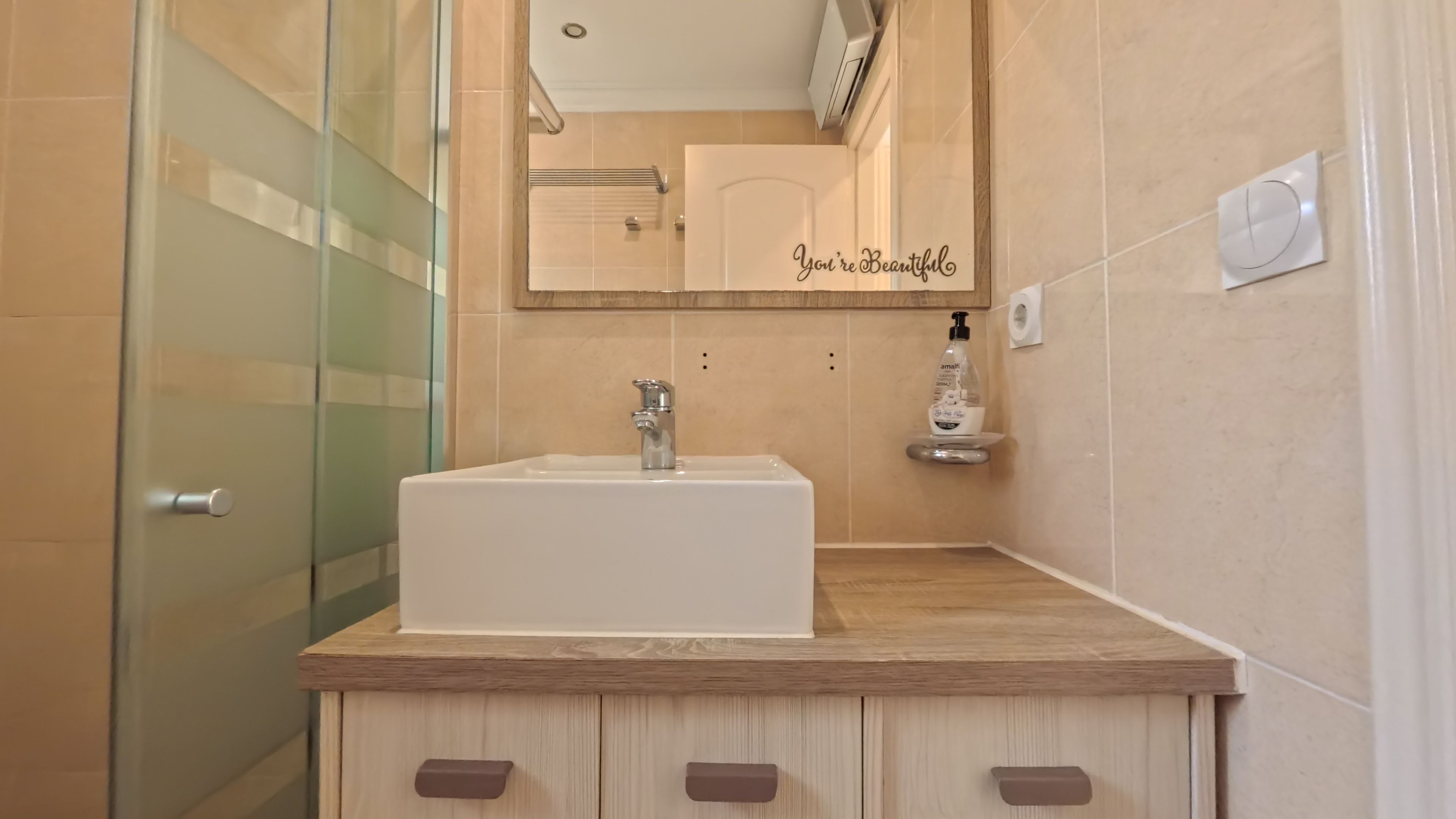 A modern bathroom with a white sink, wooden vanity, and a mirror with a motivational quote.
