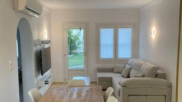 Ein modernes Wohnzimmer mit einem Holzesstisch, einem beigefarbenen Sofa und einem an der Wand montierten Fernseher.