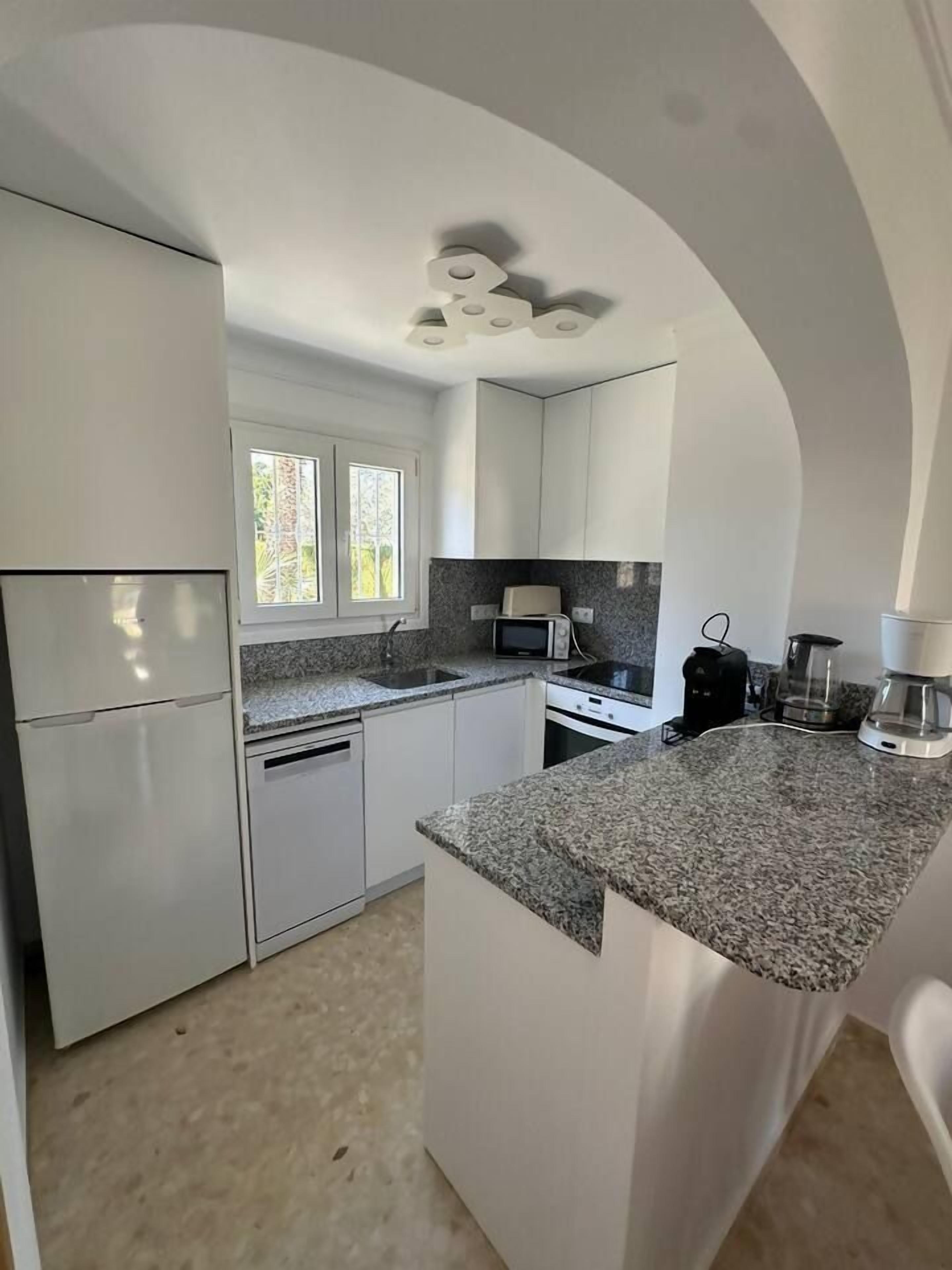 Una cocina moderna con muebles blancos, encimeras de granito y horno integrado.