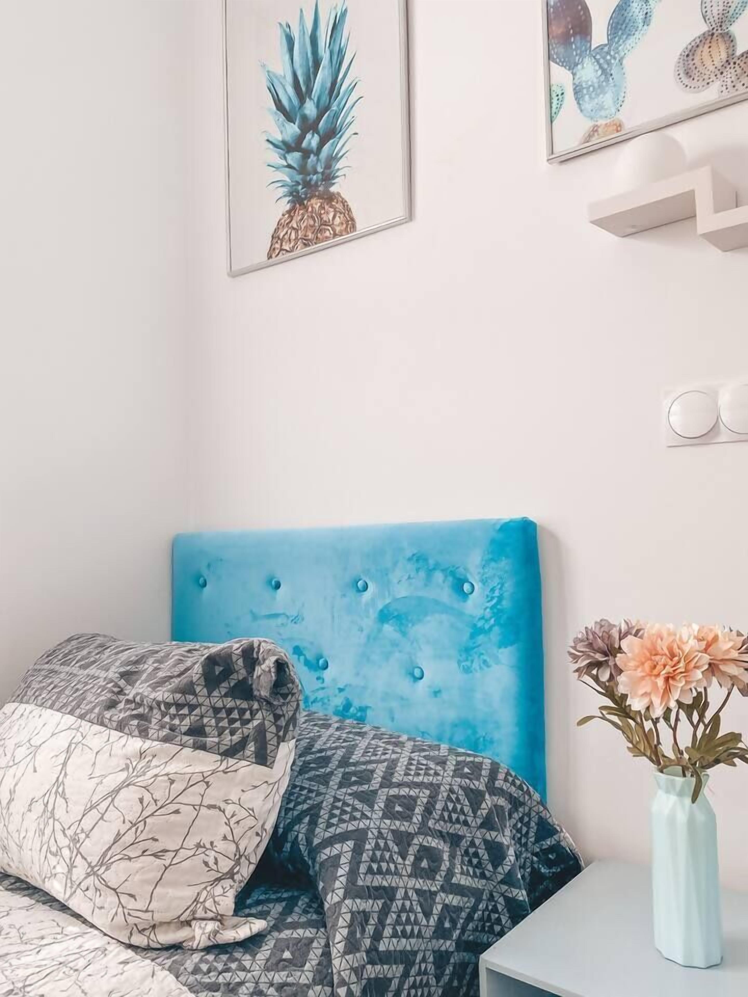 A bedroom with a blue headboard, patterned bedding, and a vase with flowers on a nightstand.