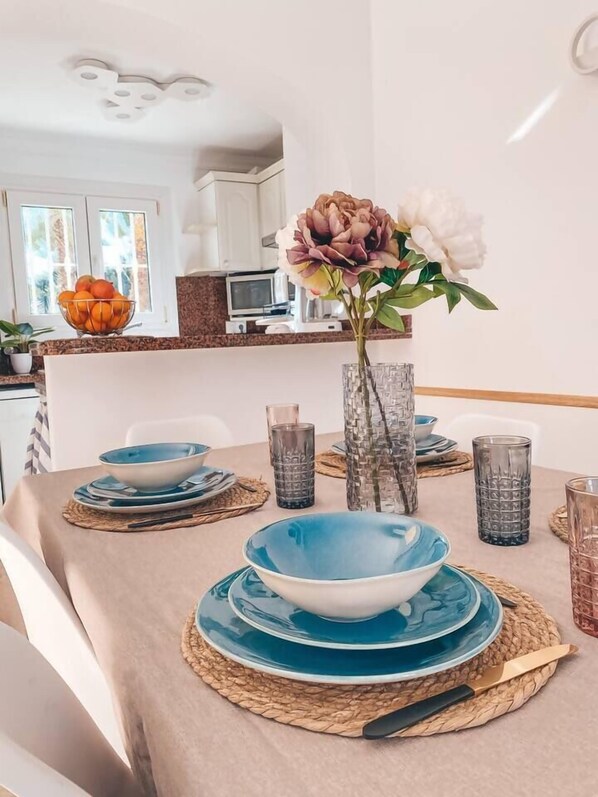 A dining table set with blue plates, a vase with flowers, and a bowl of oranges. - Brisa Azul by Midelisa. (Oliva)