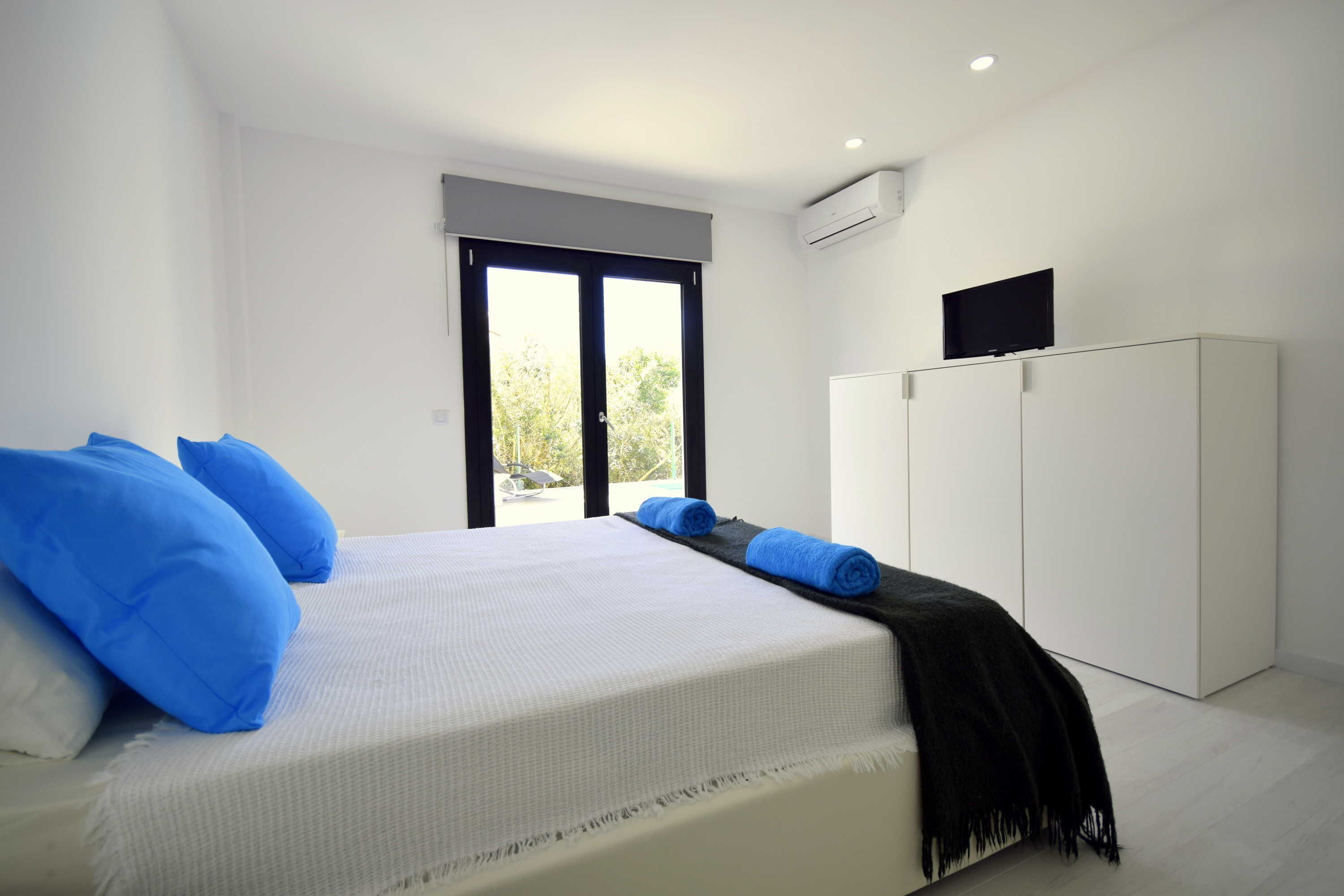 A bedroom with a bed, white walls, a large window, and a wardrobe.