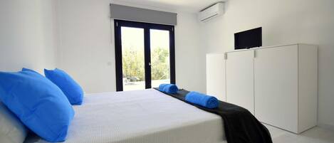 A bedroom with a bed, white walls, a large window, and a wardrobe.