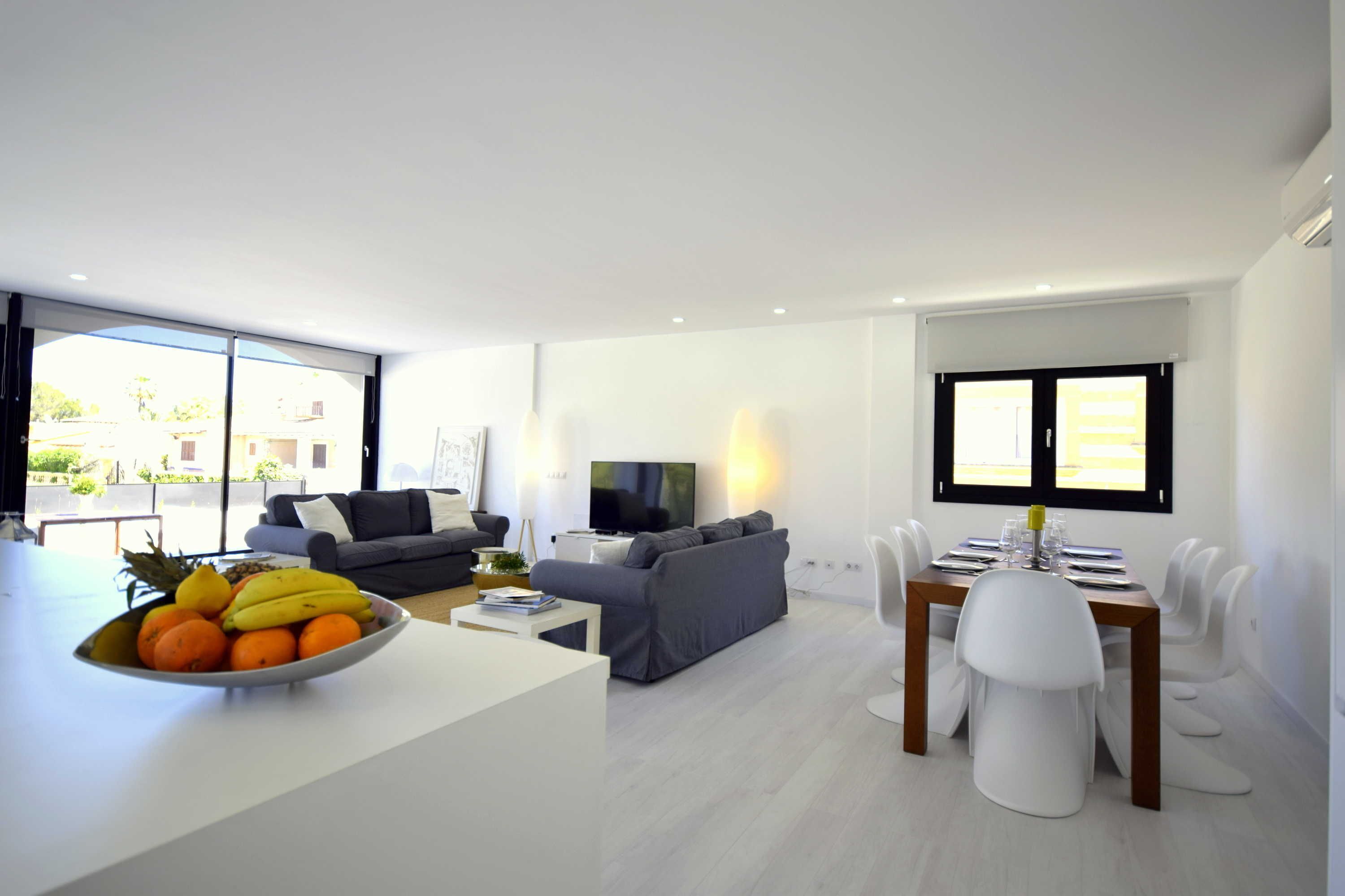A modern living room with a dining area, a large window, and a fruit bowl on the counter.