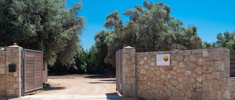 Una entrada protegida con muros de piedra y un letrero, rodeada de árboles.