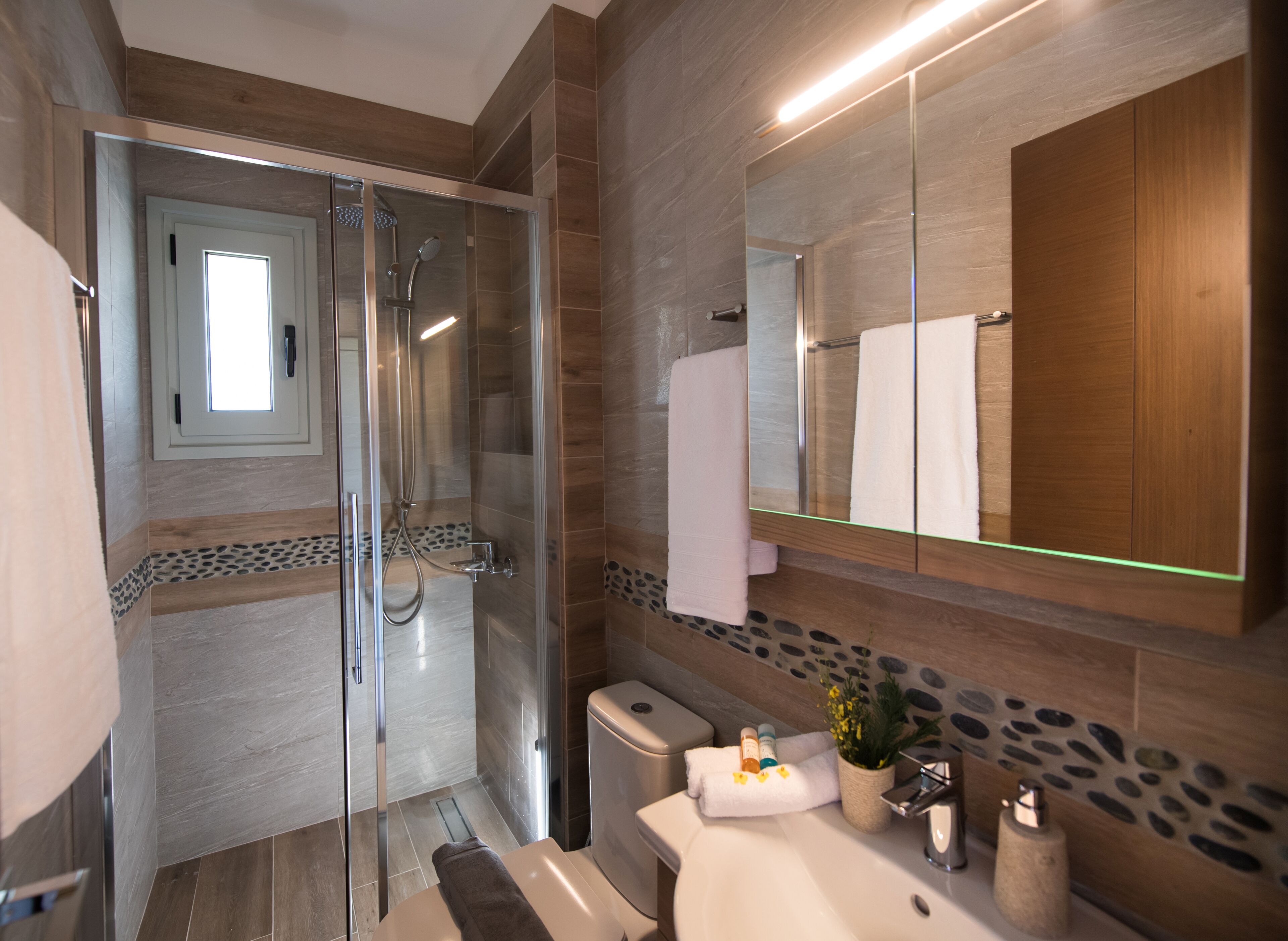A modern bathroom with a glass-enclosed shower, a large mirror, and a sink with toiletries.