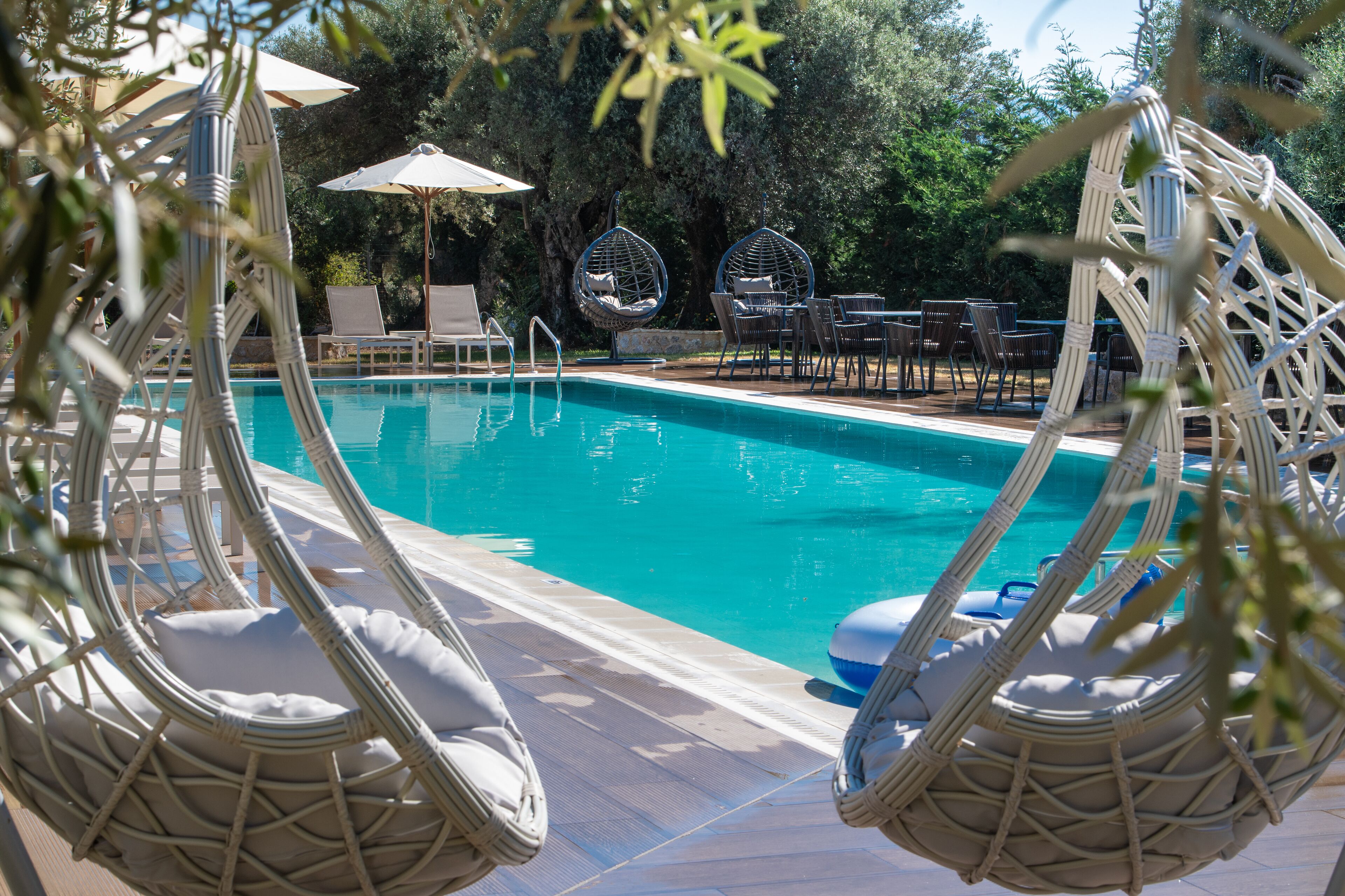 Un área de piscina con sillas de mimbre y sombrillas, rodeada de árboles.