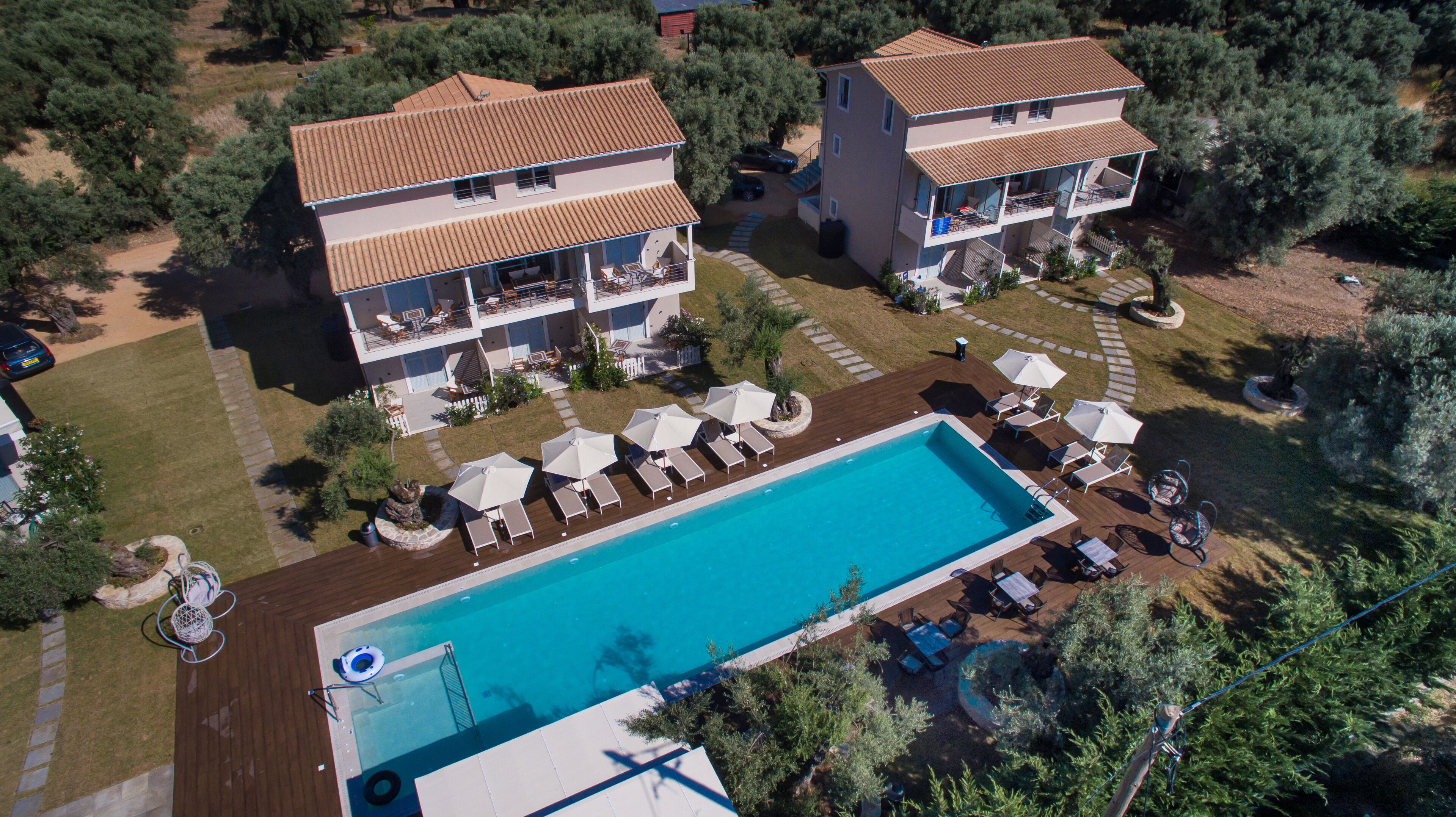 An aerial view of a resort with a swimming pool, two-story buildings, and outdoor seating areas.
