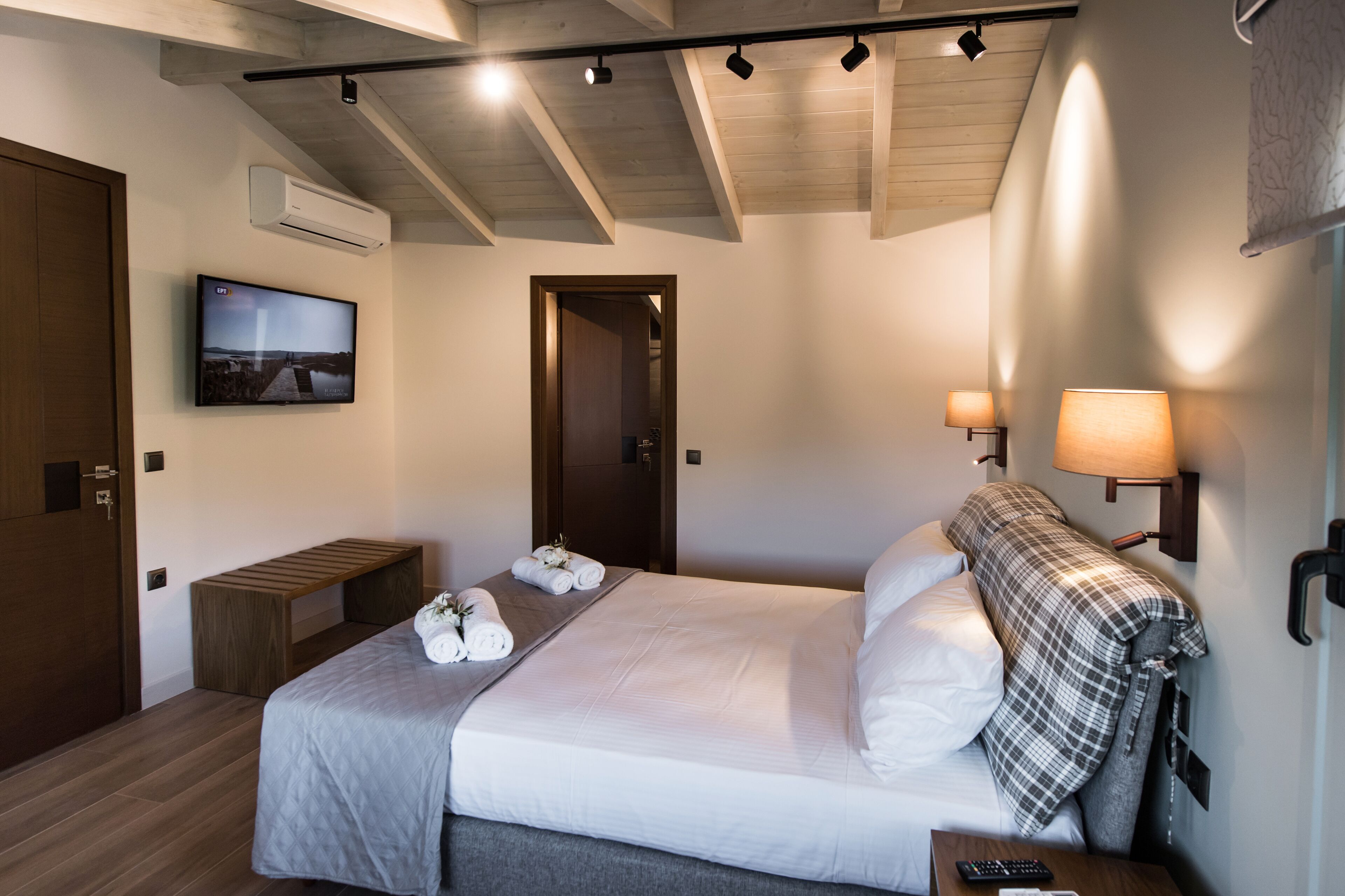 A hotel room with a bed, a bench, a TV, and a wall-mounted lamp.