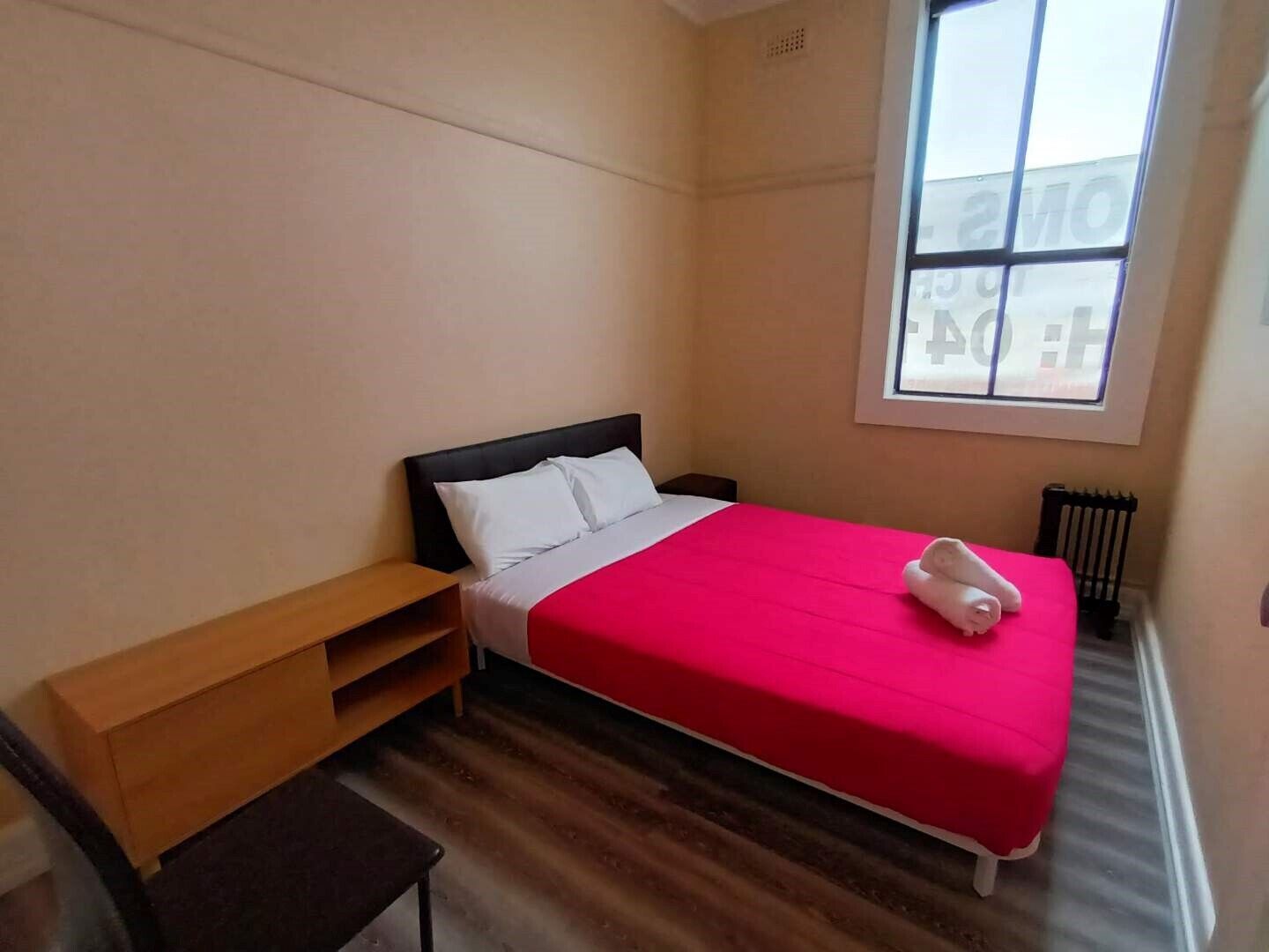 Un dormitorio con una cama, una mesita de noche de madera, un banco y una ventana.