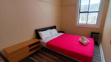 Un dormitorio con una cama, una mesita de noche de madera, un banco y una ventana.