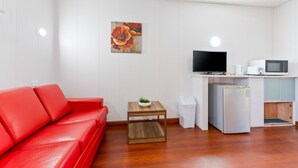 A compact living space with a red sofa, a small wooden table with a plant, a television, a microwave, and a refrigerator.