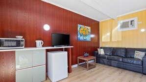 A compact living space with a kitchenette, a flat-screen TV, a sofa, and a painting on the wall.