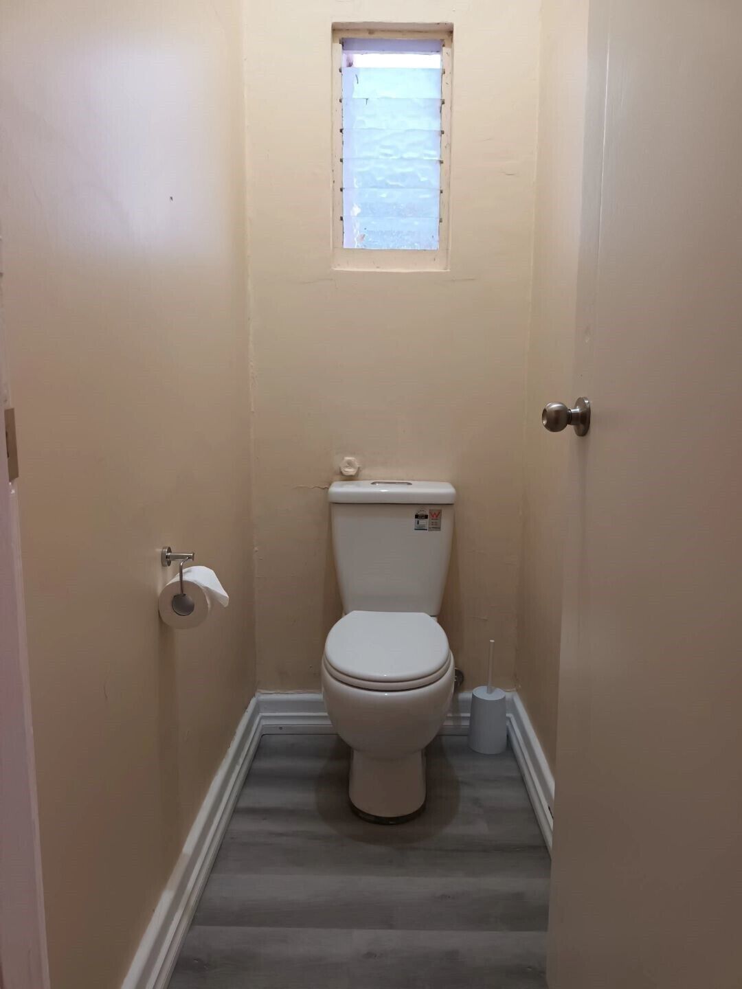 Un baño pequeño y estrecho con un inodoro, una ventana y un rollo de papel higiénico en la pared.
