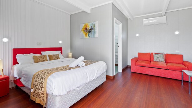 A modern hotel room with a large bed, a red sofa, and a painting on the wall.