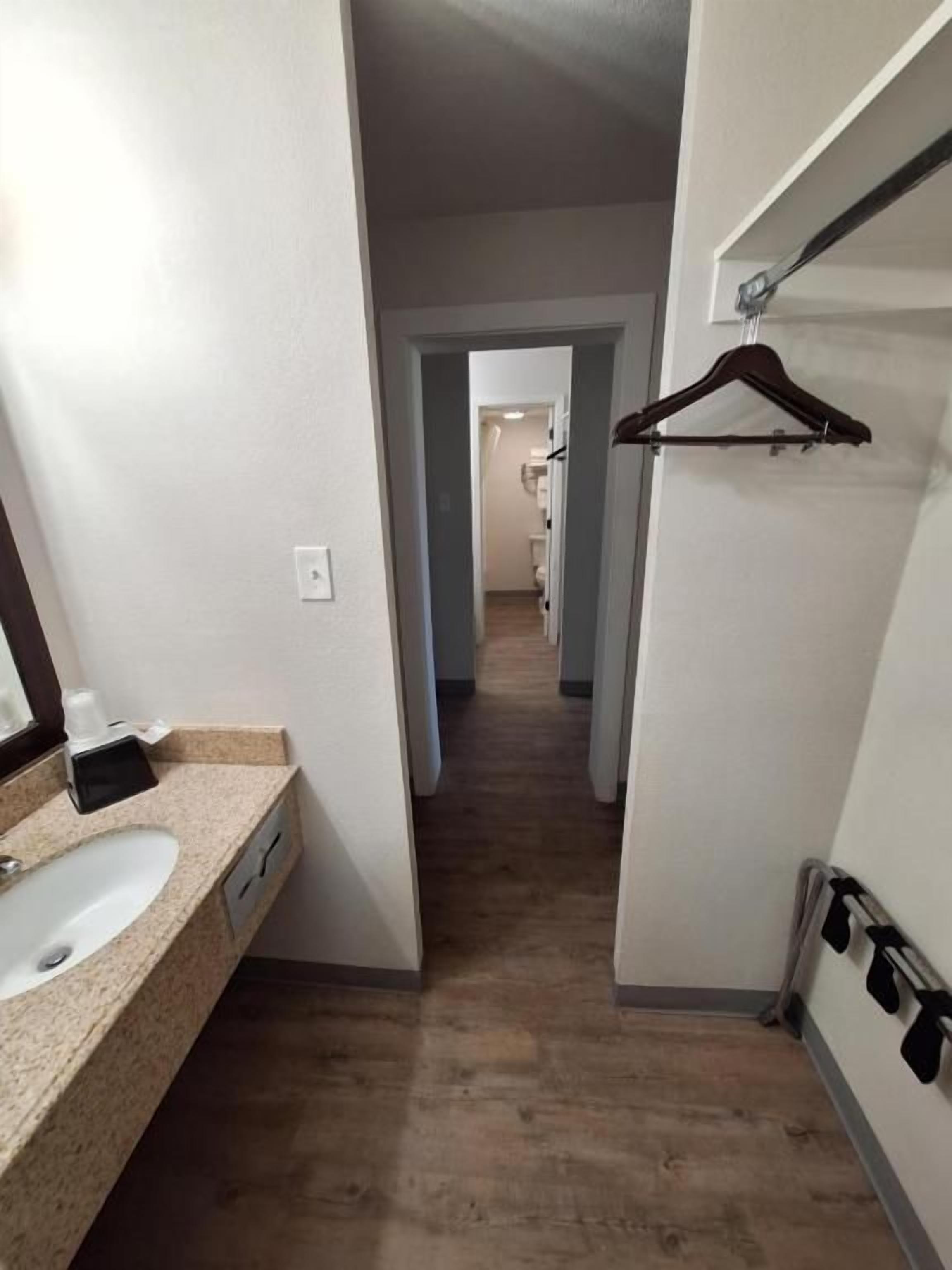 Un pasillo estrecho con un baño a la izquierda, un perchero a la derecha y una puerta que da a otra habitación.