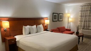 A hotel room with a large bed, two bedside lamps, a nightstand, a red chair, and a small table with a lamp. - The Hotel Orange (Orange)