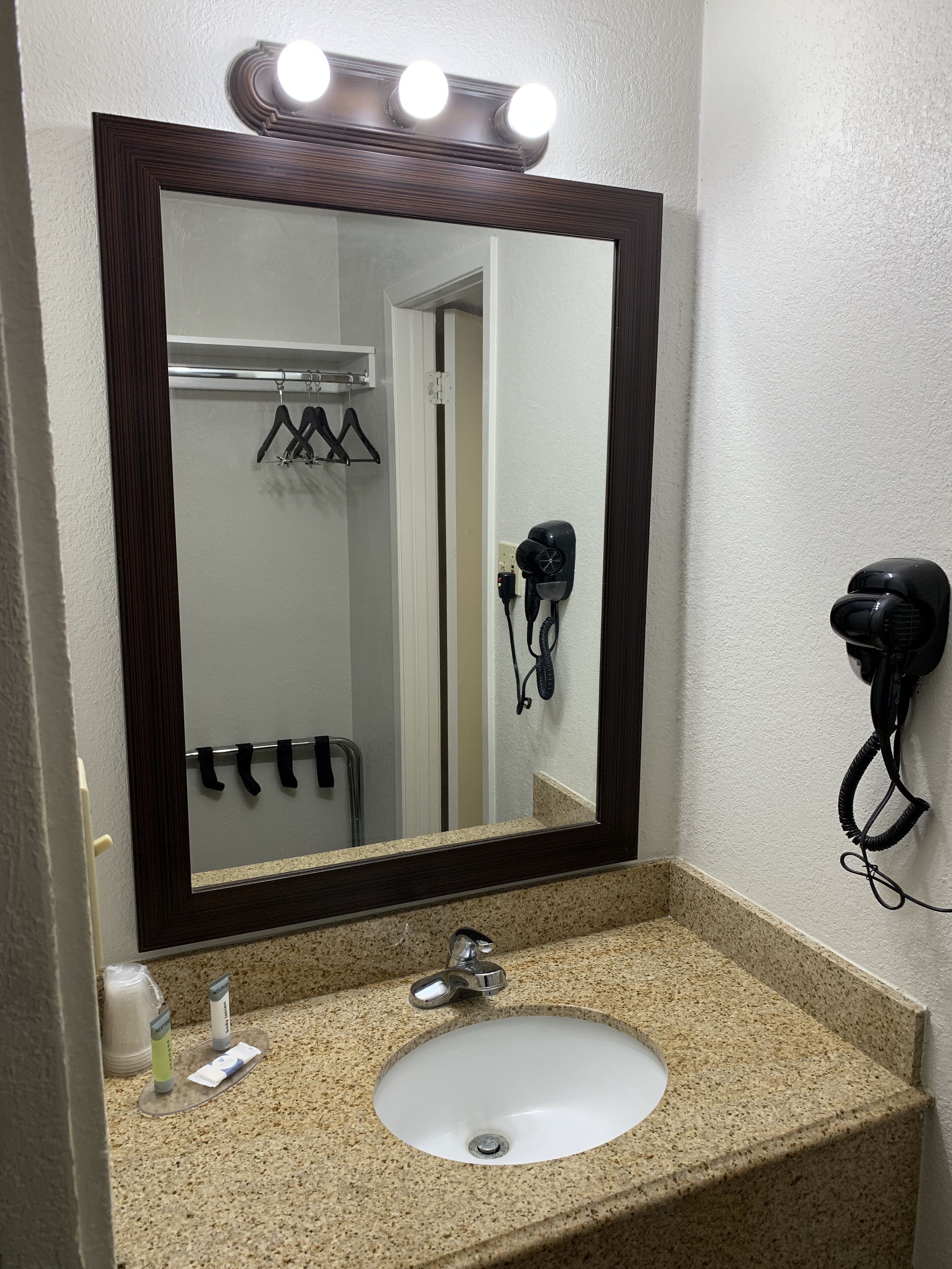 A bathroom with a large mirror, a sink, and a hairdryer mounted on the wall.