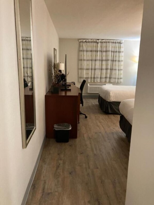 Una habitación de hotel con suelo de madera, un escritorio con silla, una cama, una ventana con cortinas y un radiador.