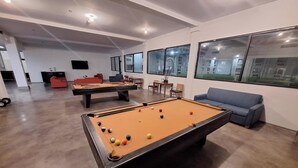 A pool table with balls, a sofa, and a billiards table in a room with large windows. - The Hotel Orange (Orange)