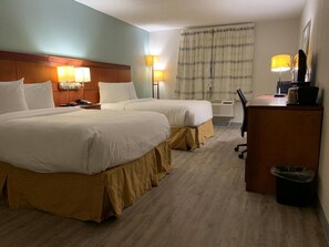 A hotel room with two beds, a desk, a trash bin, and a window with curtains.